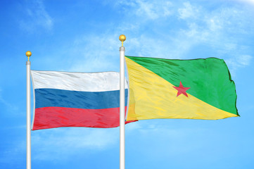 Russia and French Guiana two flags on flagpoles and blue cloudy sky