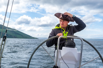 Sailboat skipper with pirate's style cocked hat at modern sailing yacht helm. Arran island, Scotland
