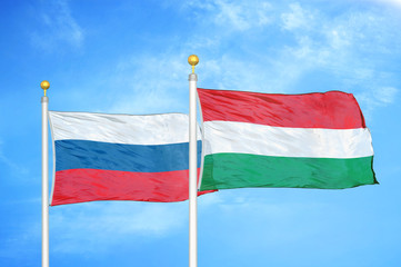 Russia and Hungary two flags on flagpoles and blue cloudy sky