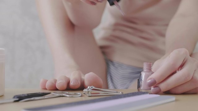 Sequence of shots of young Asian woman sitting on couch, covering foot nails with nail polish and recording voice message to friend using cellphone