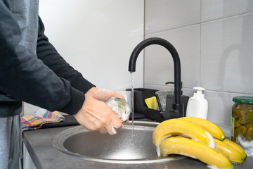 Side view on hands of unknown caucasian man person holding a can under sink tap washing food with soap cleaning disinfection in water to disinfect from viruses or pollution at home in kitchen
