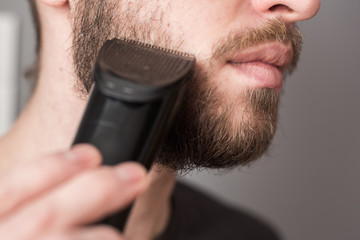 A man shaves his beard with a trimmer