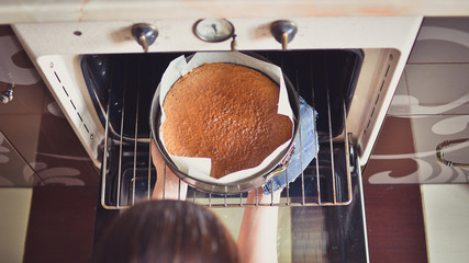 Woman hands taking out ready cake out of the the oven. 