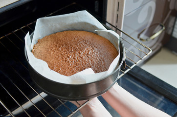 Woman hands taking out ready cake out of the the oven. 