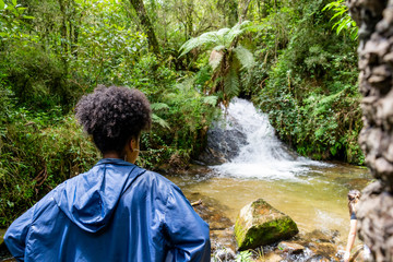 jovem observa pequena cascata de água em meio a vegetação