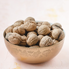 Uncracked walnuts in shell in bowl on pink background, concept of healthy eating vegan food. Close up, selective focus, copy space.