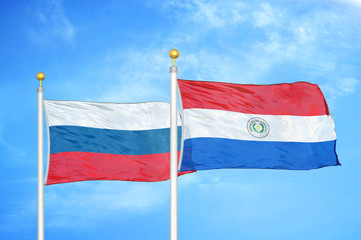 Russia and Paraguay two flags on flagpoles and blue cloudy sky