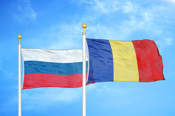 Russia and Romania two flags on flagpoles and blue cloudy sky