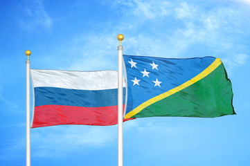 Russia and Solomon Islands two flags on flagpoles and blue cloudy sky