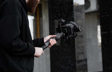 Bearded Professional videographer in black hoodie holding professional camera on 3-axis gimbal...