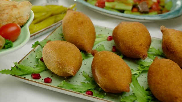 Delicious fried traditional kibbeh garnished with pomegranate and salad on a plate.