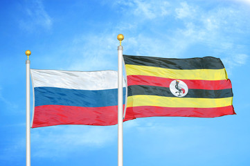 Russia and Uganda two flags on flagpoles and blue cloudy sky