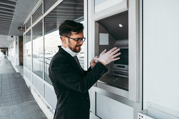 Business man with protective face mask and gloves using street ATM machine. Virus pandemic or epidemic concept.