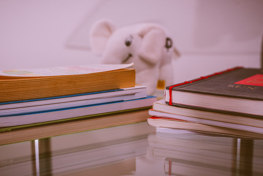 Stack Of Books And White Elephant Puff On Cristal Table