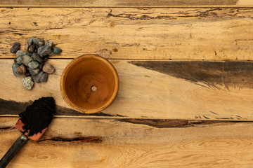 Clay pot, hand shovel with black soil and gravel on wooden background with copy space.Garden and home topic: gardening and landscaping service concept.