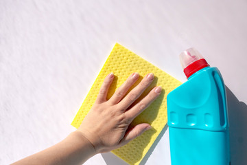 House cleaning and disinfection, prevention of coronavirus. A blue bottle of chlorine-free disinfectant and a woman's hand wiping the white surface with a cellulose cleaning cloth close-up with copy s