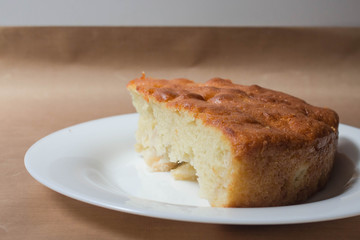 Sweet homemade cakes with apples. A slice of sponge Apple pie with a ruddy crust on a white plate close-up on a beige textile linen background.
