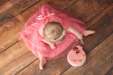 One year old baby celebrates birthday. Photo zone. Cute dress in pink color. Disgruntled little kid. Smash cake. View from above.