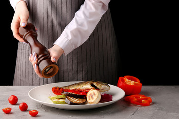 chef using pepper mill. grilled vegetables and fish. pepper. female hands of the chef. on a black background