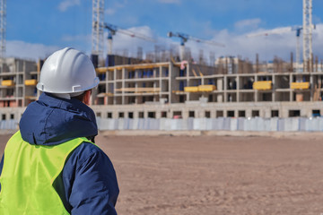 civil engineer in a white helmet and yellow vest against the background of a building under construction