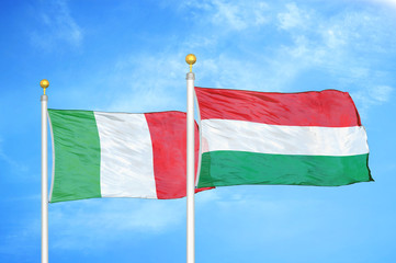 Italy and Hungary two flags on flagpoles and blue cloudy sky