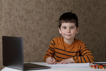 the child learns remotely through the computer. The boy draws with pencils and looks into the laptop