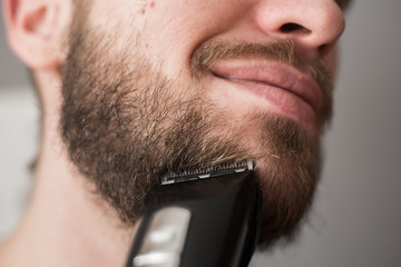Man shaves his beard with an electric trimmer - obrazy, fototapety, plakaty