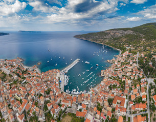 Aerial panoramic view of city Komiza - the one of numerous port towns in Croatia, is a lot of moored sailboats of a regatta, orange roofs of houses, a cathedral St.Nicholas, beach Gusarica,