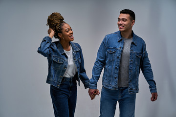 Happy girl with a guy in denim jackets and jeans walk holding hands. Relationship concept