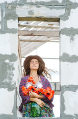An attractive girl with dark hair in a hat with red poppies in her hands in a field