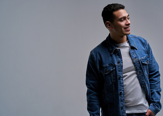 Obraz premium Glad man in a t-shirt in a denim jacket stands with his arm in jeans pocket. Fashion concept