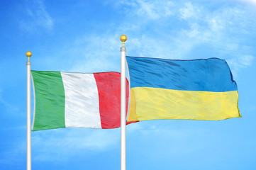 Italy and Ukraine two flags on flagpoles and blue cloudy sky