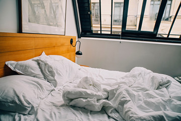 Empty messy unmade bed with white linens 