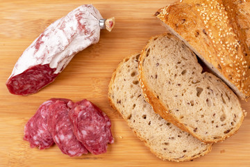 Baked sausage and several sliced sausage slices next to sliced whole grain bread on a wooden board. The concept of simple affordable food.