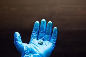 hand wearing blue latex protective gloves holding a medicine capsules up on a wooden background 