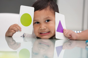 Young boy holding flash cards to learn about basic shape recognition and colors.
