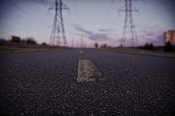 Closeup view of black asphalt road with faded dash lines in front of hydro poles and cloudy evening sky
