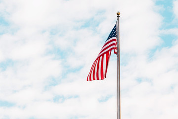 Flag of the United States of America waving on a blue sky with white clouds.