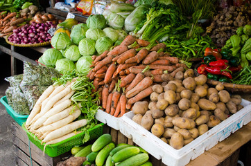 A display of vegetables in the market with radish, carrots, potatoes, cabbages, red bell peppers,...