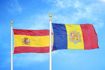 Spain and Andorra  two flags on flagpoles and blue cloudy sky