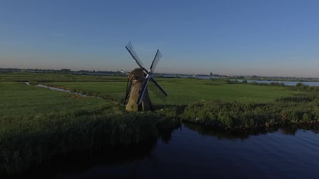 Cinematic and smooth aerial drone shot of a typical traditional dutch windmill in the green grassland during sunset