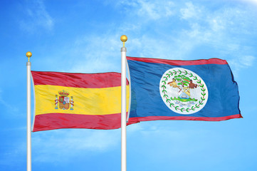Spain and Belize  two flags on flagpoles and blue cloudy sky