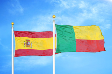 Spain and Benin  two flags on flagpoles and blue cloudy sky