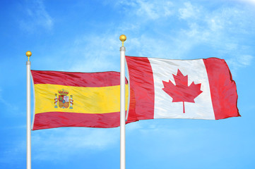 Spain and Canada  two flags on flagpoles and blue cloudy sky