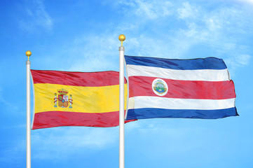 Spain and Costa Rica two flags on flagpoles and blue cloudy sky