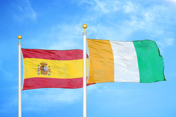 Spain and Cote d'Ivoire Ivory coast  two flags on flagpoles and blue cloudy sky