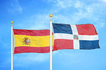 Spain and Dominican Republic two flags on flagpoles and blue cloudy sky