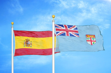 Spain and Fiji two flags on flagpoles and blue cloudy sky