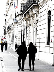 A silhouette view of a pair of people walking through the city from the back. A photo processed in a photo editor with a black and white effect.
