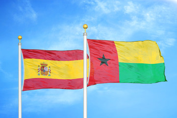 Spain and Guinea-Bissau two flags on flagpoles and blue cloudy sky